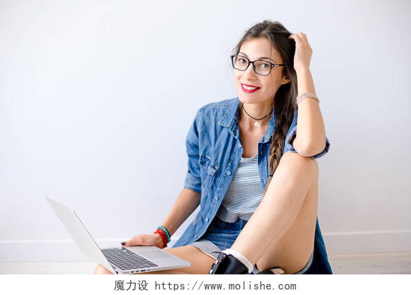 特写肖像的微笑的女人穿着牛仔服装手持笔记本电脑在她交叉的腿上